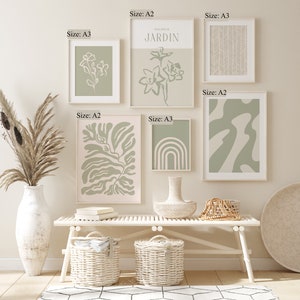 May include: A gallery wall with eight framed prints in various sizes and designs. The prints feature abstract shapes, botanical illustrations, and geometric patterns in shades of green and white. The prints are hung on a white wall above a white bench with two wicker baskets.