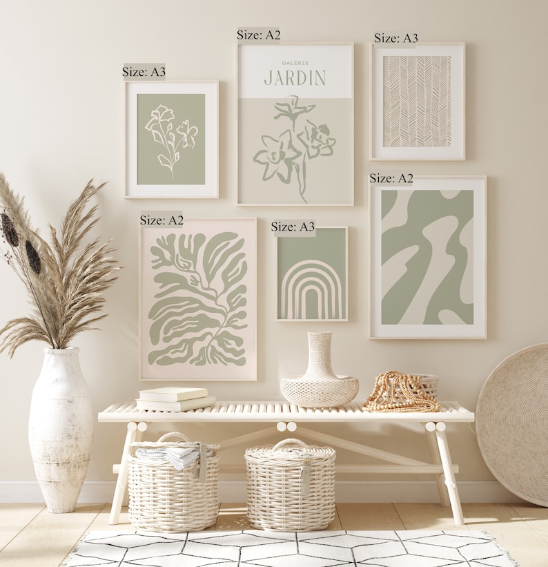 May include: A gallery wall with eight framed prints in various sizes and designs. The prints feature abstract shapes, botanical illustrations, and geometric patterns in shades of green and white. The prints are hung on a white wall above a white bench with two wicker baskets.