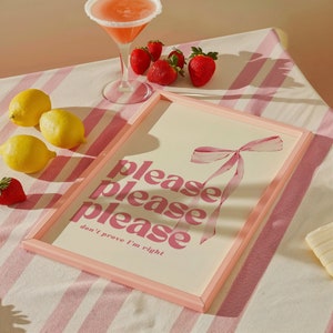 May include: Pink framed print with the text "please please please don't prove I'm right" in pink lettering. A pink ribbon is in the background.