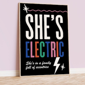 Op de afbeelding: Zwart-witte poster met de tekst "She's Electric" in kleurrijke letters. De tekst "She's in a family full of eccentrics" staat onder de hoofdtekst met een bliksemgrafiek.