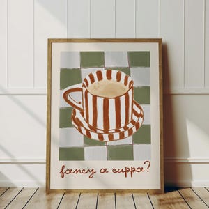 May include: A framed art print featuring a coffee cup and saucer with brown and white stripes, set against a green and white checkered background. The phrase "fancy a cuppa?" is written in brown script at the bottom.