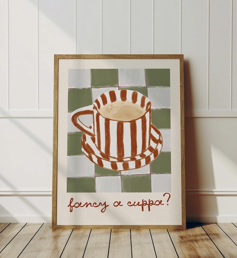 May include: A framed art print featuring a coffee cup and saucer with brown and white stripes, set against a green and white checkered background. The phrase "fancy a cuppa?" is written in brown script at the bottom.