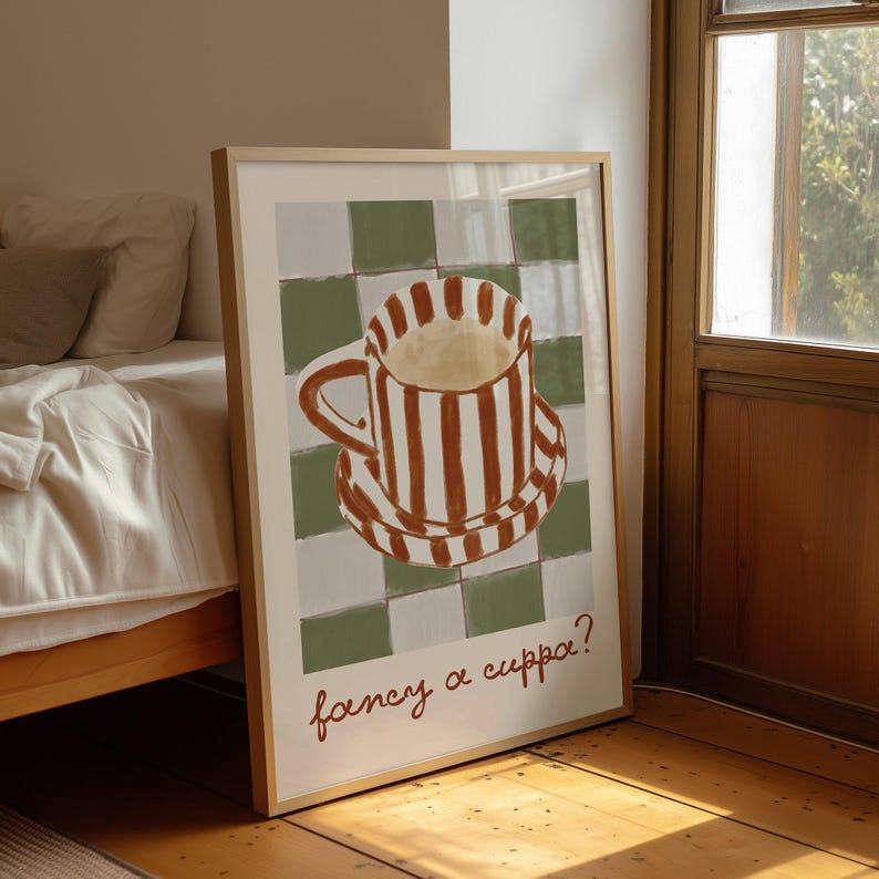 May include: A framed art print featuring a whimsical illustration of a striped coffee cup and saucer. The cup and saucer are brown and white striped, set against a green and white checkered background. The text "fancy a cuppa?" is written in brown script.