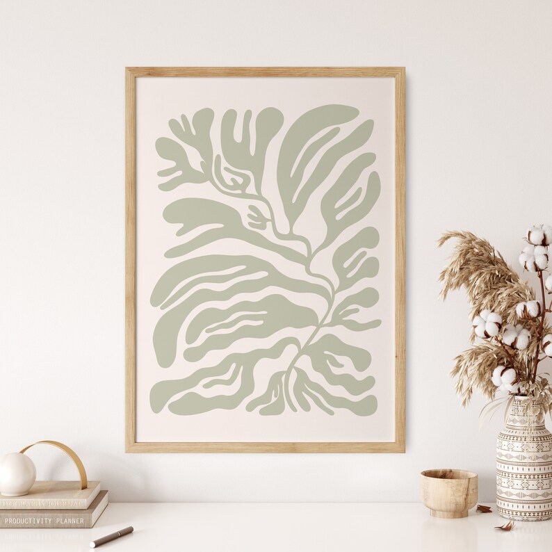 May include: A framed print of a green abstract leaf design on a white background. The frame is made of light wood.