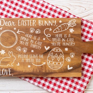 May include: A wooden cutting board with a white design that says "Dear Easter Bunny" and includes a place for a drink, a treat, and a message for the Easter Bunny. The board is on a red and white checkered tablecloth.
