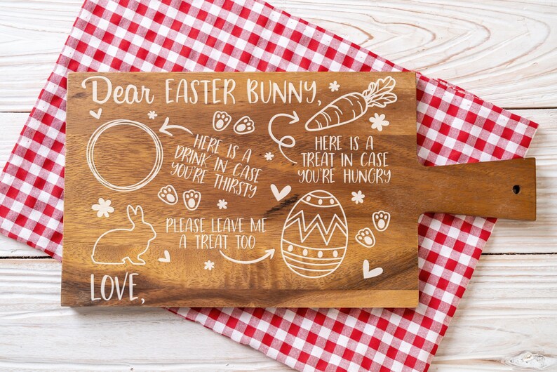 May include: A wooden cutting board with a white design that says "Dear Easter Bunny" and includes a place for a drink, a treat, and a message for the Easter Bunny. The board is on a red and white checkered tablecloth.