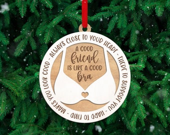 May include: A round wooden ornament with a white cutout of a bra in the center. The text reads: A GOOD friend IS LIKE A GOOD bra. The outer white border features the text: ALWAYS CLOSE TO YOUR HEART - THERE TO SUPPORT YOU - HARD TO FIND - MAKES YOU LOOK GOOD.