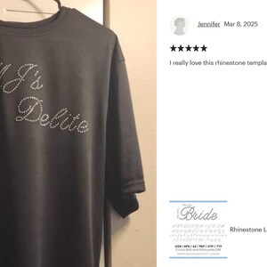 May include: A dark gray short-sleeved t-shirt featuring the text MJ's Sugar Delite spelled out in small, clear, reflective rhinestones arranged in a cursive script font across the chest area of the garment.