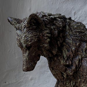 May include: A ceramic sculpture of a wolf, with a textured, bark-like surface. The wolf is brown and green, with a detailed face and a slightly hunched posture.