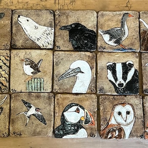 May include: A collection of 16 ceramic tiles, each featuring a different animal or bird. The tiles are painted in a variety of colours and styles, and they are all set against a light brown background.