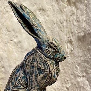 Op de afbeelding: Een blauwe en grijze keramische sculptuur van een konijn met gedetailleerde gravures. De oren van het konijn zijn lang en puntig, en zijn ogen zijn groot en alert.