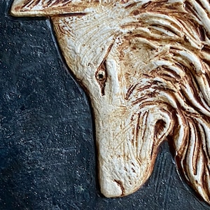 May include: A white ceramic wolf sculpture with brown accents, set against a dark blue background. The wolf's head is tilted down, and its eye is visible.