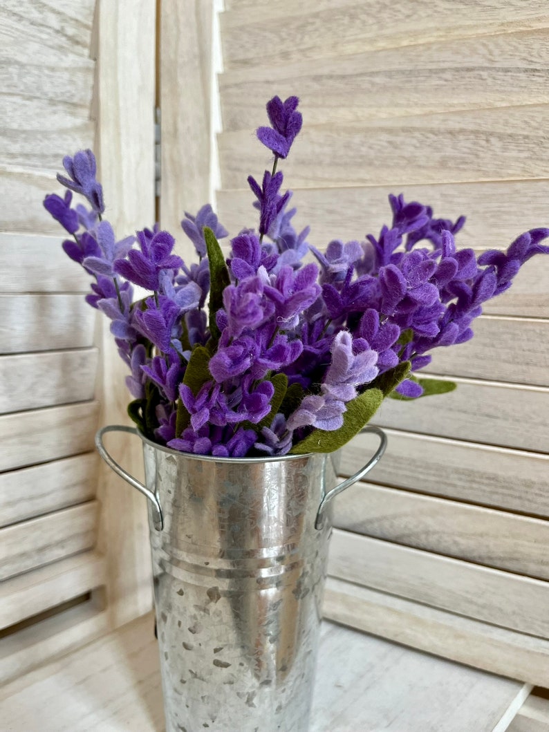 May include: A bouquet of purple lavender flowers in a galvanized metal vase with handles.