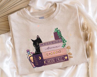 May include: A beige t-shirt with a black cat, a stack of books, a potion bottle, and a mug with a moon and stars design. The books have the words "Dream", "luna", "(∞∞∞)", and "Moon Cycle" on them.