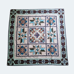 May include: A quilt with a patchwork design featuring a variety of blue, brown, and white geometric shapes. The quilt is framed by a dark brown border with a repeating pattern.
