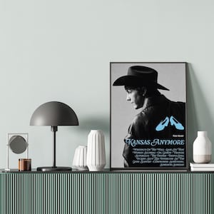 Peut inclure: Affiche encadrée en noir et blanc avec une personne portant un chapeau de cowboy, le texte "Kansas Anymore" et des paroles de chanson. L'affiche a un cadre noir et est affichée sur un meuble vert.