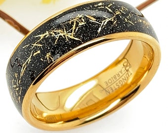 Op de afbeelding: Een gouden ring van wolframcarbide met een zwarte en gouden gespikkelde afwerking. De ring heeft de woorden "Tungsten Carbide" gegraveerd aan de binnenkant.