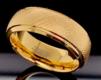 May include: A gold tungsten carbide ring with a brushed finish. The ring has a beveled edge and is engraved with "Tungsten Carbide".