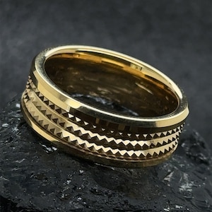 Puede incluir: Un anillo dorado con un diseño texturizado y acanalado. El anillo tiene tres bandas de canales.