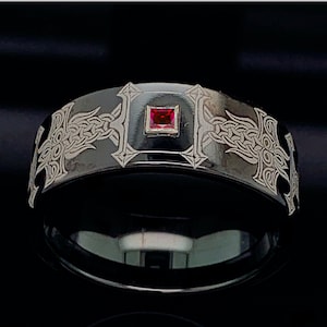 May include: A black tungsten carbide ring with a Celtic knot design and a red gemstone in the center.