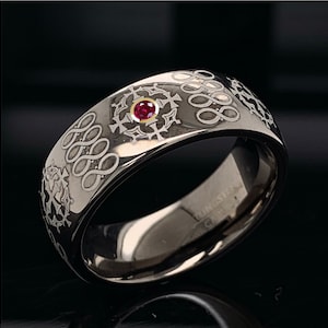 May include: A silver ring with a red gemstone and an intricate design of crosses and infinity symbols.