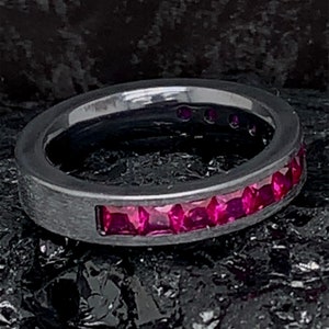 May include: A black titanium ring with a row of pink gemstones set into the band.
