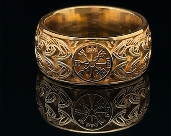 May include: A gold-toned ring with a Celtic knot design and a central circular symbol. The symbol features a compass-like design with eight points.