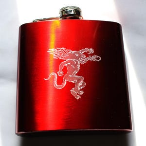 Könnte beinhalten: Rote Metallflasche mit silbernem Verschluss und einem weißen, gravierten Bild eines feurigen Dämons.