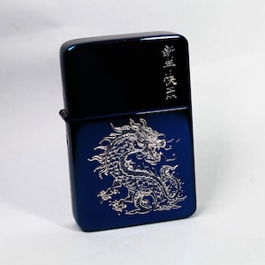 May include: A blue metal lighter with a silver dragon design and Japanese text. The lighter has a textured surface.