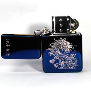 May include: A blue lighter with a silver dragon design engraved on the front. The lighter has a silver hinge and a silver wheel on the side.