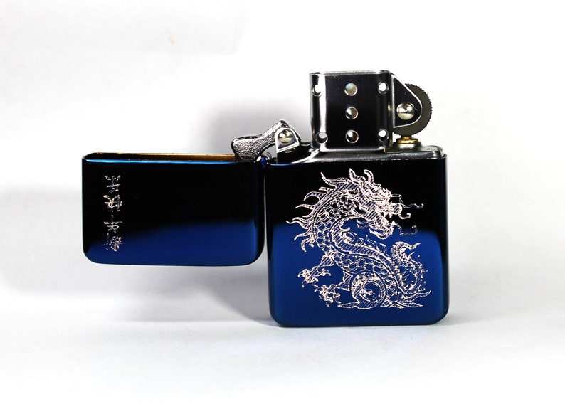 May include: A blue lighter with a silver dragon design engraved on the front. The lighter has a silver hinge and a silver wheel on the side.