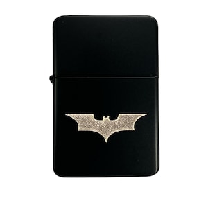 Może przedstawiać: Czarny zapalniczka z srebrnym logo Batmana.