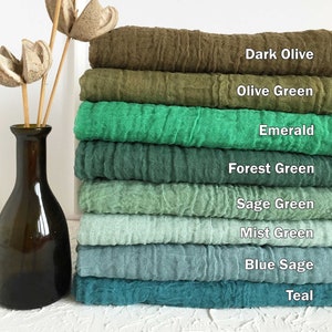 May include: A stack of eight fabric squares in various shades of green and blue, from dark olive to teal. The fabric squares are arranged from darkest to lightest, with the names of each color written below each square.