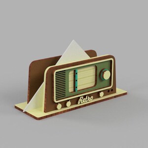 May include: A wooden napkin holder shaped like a vintage radio. The radio is brown with a green front panel and a white paper napkin inside. The radio has a dial with the word "Retro" on it.