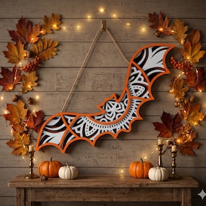 Peut inclure: Décoration murale en forme de chauve-souris pour Halloween, avec un contour orange et un motif intérieur blanc et noir. La scène comprend des citrouilles, des bougies et des feuilles d'automne, pour une ambiance festive.