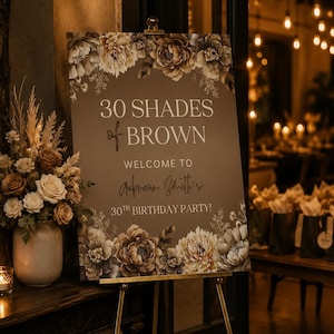 Puede incluir: Un letrero rectangular de fiesta de cumplea&ntilde;os sobre un caballete de metal dorado con fondo marr&oacute;n y texto en blanco y cursiva que dice 30 SHADES of BROWN WELCOME TO Aubreon Smith's 30TH BIRTHDAY PARTY! decorado con ilustraciones florales.