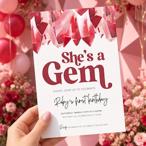 Pode incluir: Um cartão de convite de aniversário retangular com uma ilustração em aquarela de cristais vermelhos e rosas no topo. O texto diz: She's a Gem, PLEASE JOINS US TO CELEBRATE, Ruby's first birthday, SATURDAY, MARCH 10TH AT 5:00PM, 1234 PARTY LN, CELEBRATION FL 12345, RSVP BY MARCH 1ST TO CINDY AT 555.123.4567.