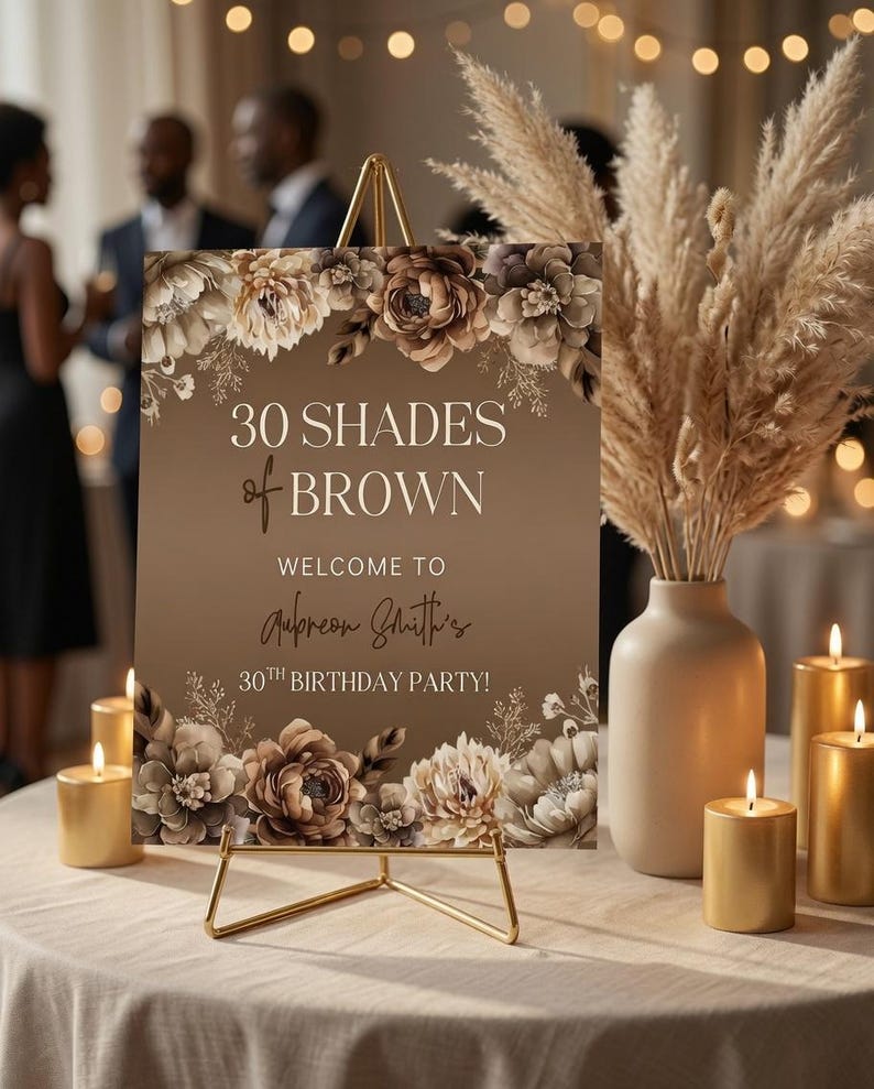 Puede incluir: Un letrero rectangular sobre un caballete de metal dorado con ilustraciones florales marrones y el texto 30 SHADES of BROWN WELCOME TO Aubreon Smith's 30TH BIRTHDAY PARTY. El letrero se muestra con velas doradas y un jarr&oacute;n con hierba.
