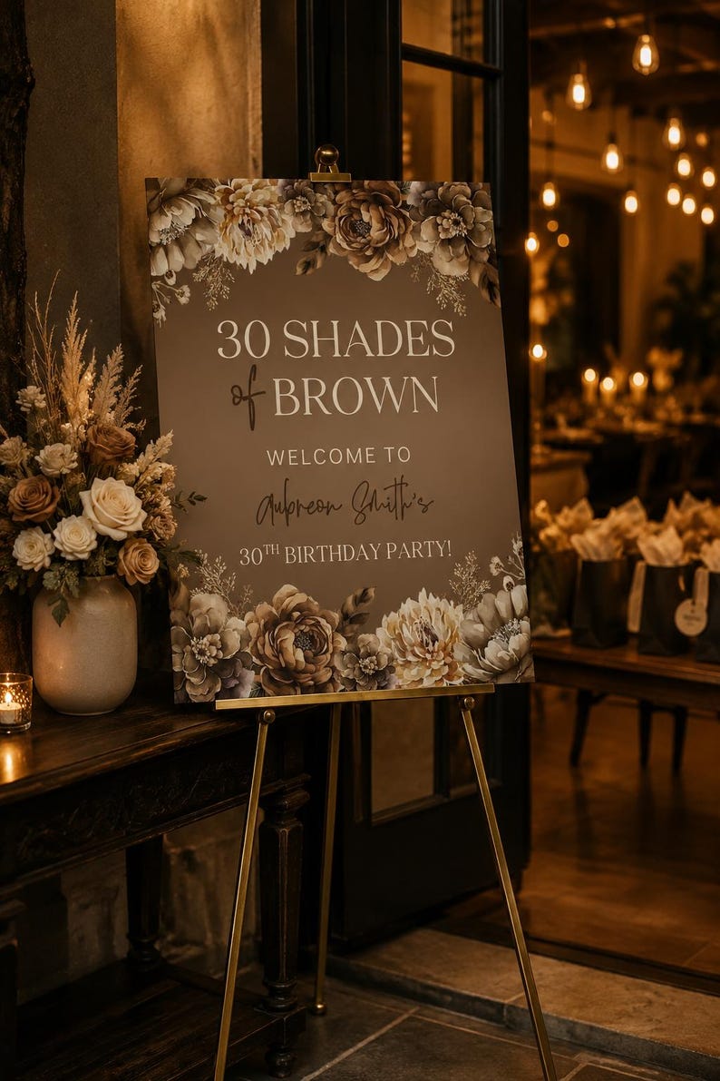 Puede incluir: Un letrero rectangular de fiesta de cumplea&ntilde;os sobre un caballete de metal dorado con fondo marr&oacute;n y texto en blanco y cursiva que dice 30 SHADES of BROWN WELCOME TO Aubreon Smith's 30TH BIRTHDAY PARTY! decorado con ilustraciones florales.