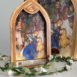 Könnte beinhalten: Ein dekoratives, mehrschichtiges Kunstwerk mit einer Fantasieszene mit Figuren in blauer, grüner und weißer Kleidung. Das Kunstwerk hat einen Holzrahmen mit einem gewölbten oberen Teil und einem Triforce-Symbol. Eine Girlande aus weißen Rosen und grünen Blättern schmückt die Basis.