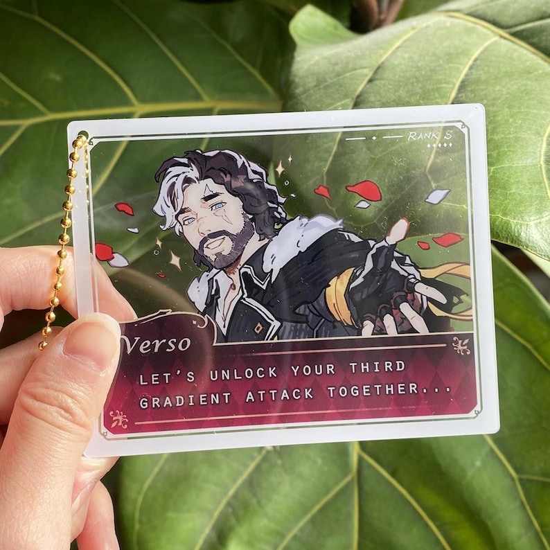 Op de afbeelding: Een heldere acryl bedel met een gouden ketting. De bedel toont een mannelijk anime-personage met zwart en wit haar, een baard en een zwart-gouden outfit. De tekst "Verso" en "Let's unlock your third gradient attack together..." zijn zichtbaar.