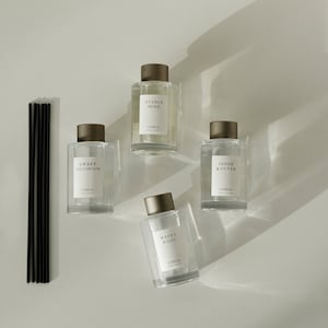 May include: Four clear glass bottles with brown caps and labels. The bottles are filled with a clear liquid and have black stick diffusers. The labels read "Stable Mind", "Sweet Optimism", "Inner & Outer", and "Happy Body". All bottles have the word "Camellia" printed on the label.