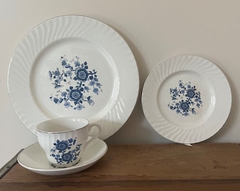 Puede incluir: Un juego de porcelana con estampado floral azul y blanco incluye una taza de té, un platillo y dos platos. Los platos tienen un borde ondulado elevado.