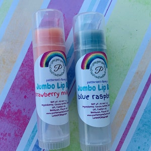 May include: Two lip balm tubes with rainbow labels. The left tube is orange and says "Jumbo Lip Balm Strawberry Milk". The right tube is blue and says "Jumbo Lip Balm Blue Raspberry". Both tubes have a net weight of 15 oz/4 g.