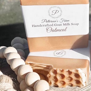 May include: Two bars of handcrafted goat milk soap, one with a label that reads "Patterson's Farm Handcrafted Goat Milk Soap Oatmeal". The soap is a light peach color and has a honeycomb pattern on the top.