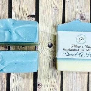 May include: Two bars of blue goat milk soap. The bar on the right has a label that reads "Patterson's Farm Handcrafted Goat Milk Soap Shave & A Haircut".