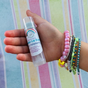 May include: A clear tube of lip balm with a rainbow label that reads "Patterson's farm jr.  Jumbo Lip Balm Blue raspberry  wt. .15 oz / 4.3 g Ingredients: Cocoa butter, Coconut oil, Castor oil,  Beeswax, Flavor oil.  www.pattersonfarmjr.com  LoveYa'sLipBalms"