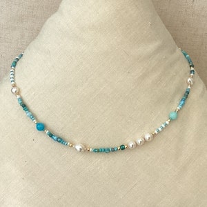 May include: A delicate necklace made with small turquoise and white beads, accented with larger turquoise and white pearls.