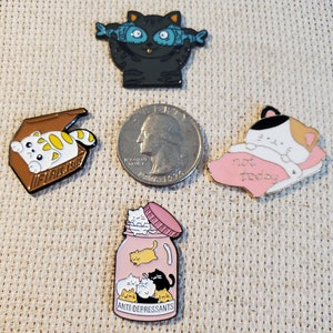 May include: A collection of cat-themed enamel pins. One pin features a black cat with fish-shaped eyes, another shows a cat in a box, and a third depicts a cat on a pillow with the text "not today". A jar pin reads "ANTI DEPRESSANTS".