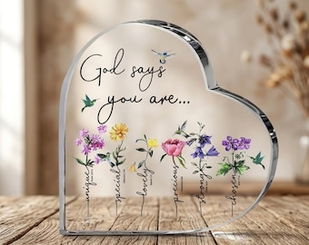 May include: A heart-shaped clear acrylic plaque featuring the text God says you are... followed by six floral illustrations with the words unique, special, lovely, precious, strong, and chosen, each paired with small hummingbird graphics.